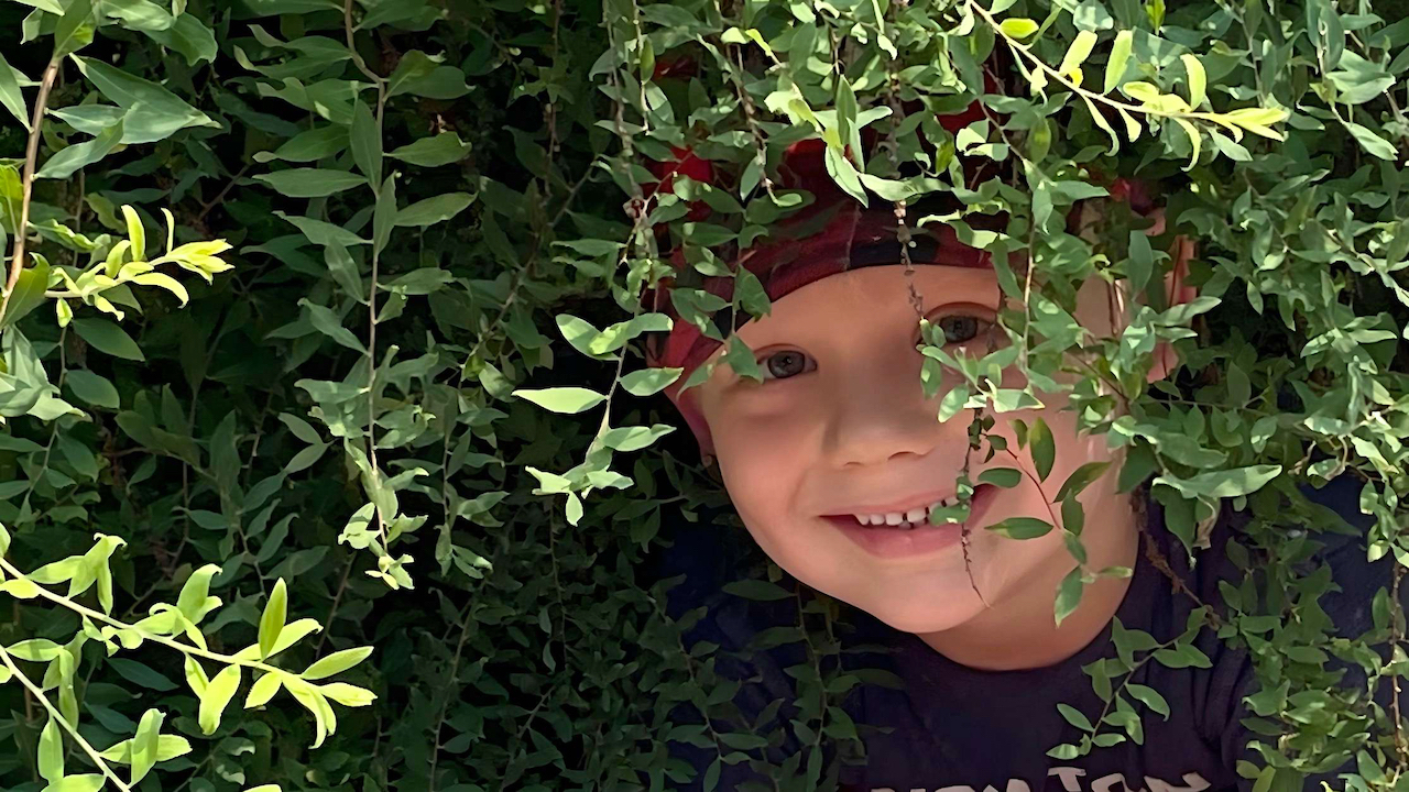Nature Based Learning - Boy Peeking Out from Under a Bush