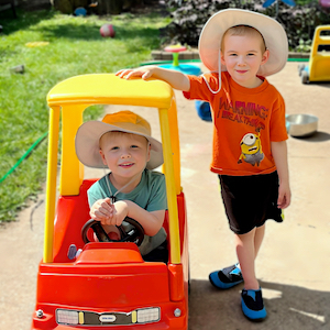 Child Care Safety - Boy in sun hat standing next to a boy in a play car